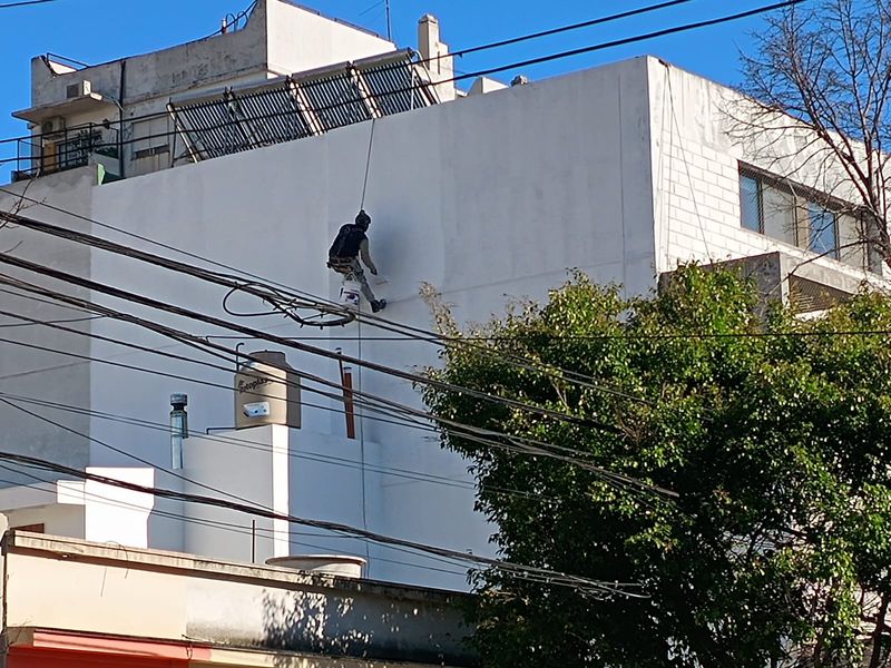Técnico en acceso por cuerdas aplicando impermeabilizante en medianera de Villa Urquiza